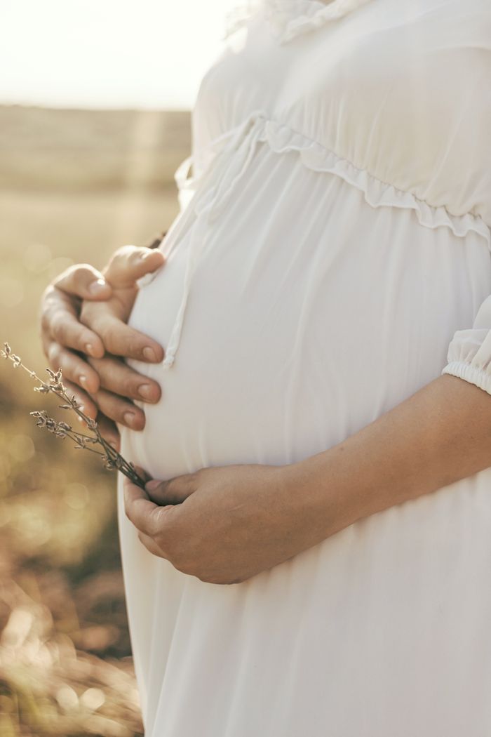 A serene close-up shot of a pregnant woman holding her belly gently in a sunlit outdoor setting.